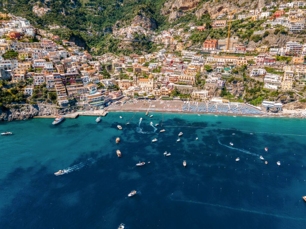 Aerial drone view of the Tyrrhenian sea coast in Positano, Italy. Multiple classic buildings on rocky cliffs, a lot of greenery