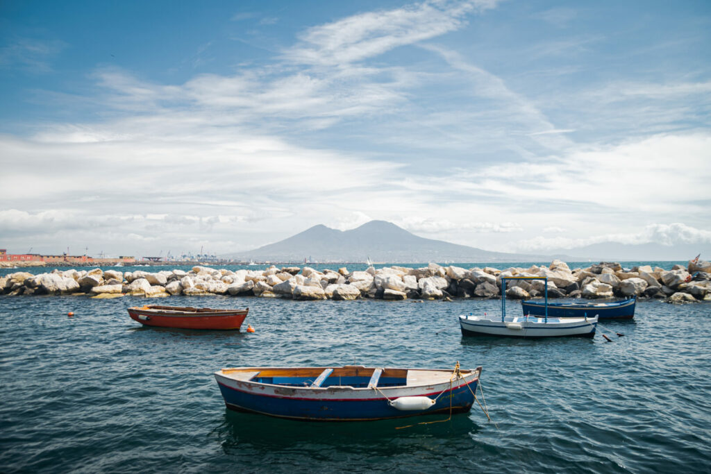 Calm blue Tyrrhenian Sea. View from the embankment of Naples to Mount Vesuvius volcano. Pleasure boats moored near the shore and stone breakwaters. Beautiful landscape for meditation